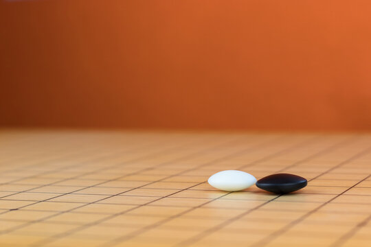 Black and white stones on the playing field (gohan) of Chinese game go, orange background