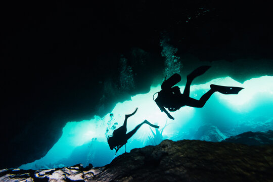 Silhouette of scuba divers diving in a dark underwater cave