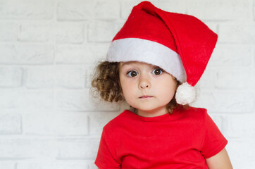 portrait of surprised little cute girl in red suit and santa hat for christmas. emotional child on new year looking at the camera. copy space, place for text