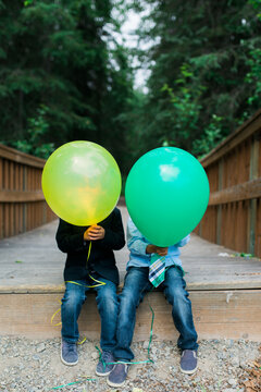 two young boys hide their faces behind balloons