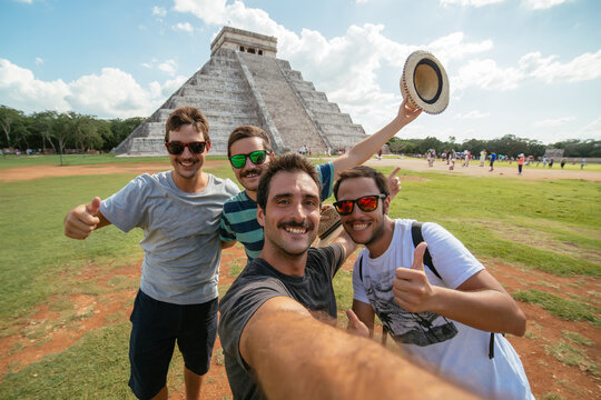 Young group of friends wearing sunglasses taking a selfie in front of Kukulkan pyramid in Chichen Itza, Mexico