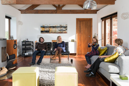 Family in a contemporary living room with daughter playing the violin.