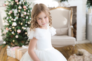 little beautiful girl in a white fluffy, elegant dress on the background of Christmas trees in the interior of the home. new year holidays and vacations.