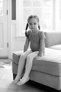 Cute young girl sitting on an ottoman in a ballet outfit