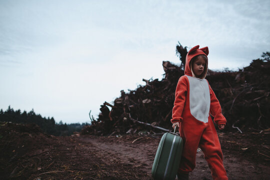 Child in fox costume walking with suitcase near logging site