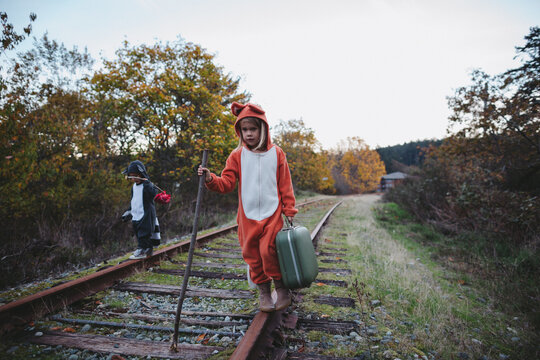 Kids dressed up like fox and raccoon walking on train tracks