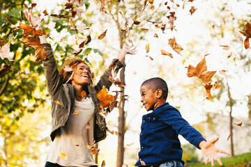 Mother and her son playing with autumn leaves in the park.