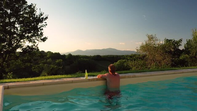 Aerial view of young male adult relaxing swimming pool panoramic scene at sunset in tuscany italy shot in 4k