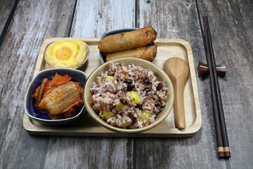 Traditional breakfast set, cooked jasmine rice with bean, gingko, mixed grains and shrimp serving with pickled vegetable (kimchi), fried sprig roll and sweet dessert on the wooden plate.