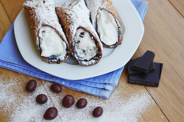 Traditional italian pastry called Cannolo with candied fruit and chocolate on a plate on wooden...