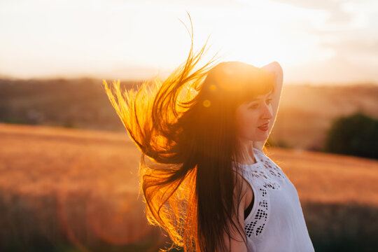 A brunette lady flicks her hair back, it is back lit by the sunset