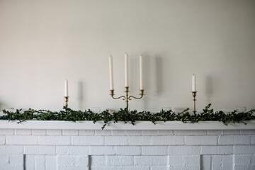 Green garland on white brick fireplace mantle with candle sticks for the holidays