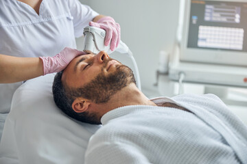 Obraz na płótnie Canvas Doctor beautician treating male skin with laser device