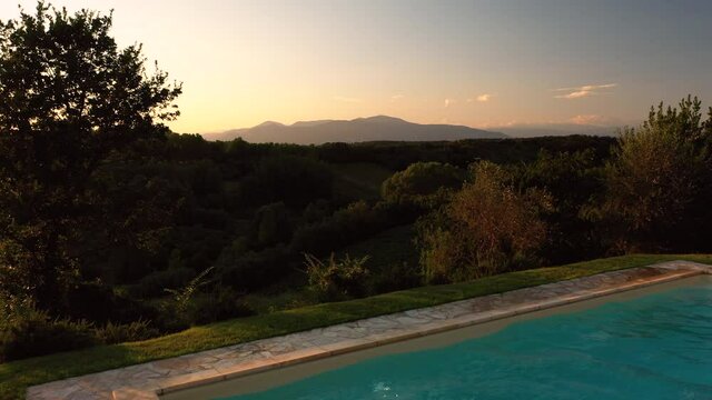 Aerial view of young male adult jumping swimming pool panoramic scene at sunset in tuscany italy shot in 4k