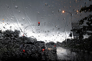 Water droplets on the windshield of the car against a background of cloudy sky and traffic lights