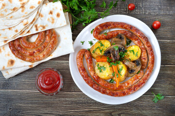 Tasty homemade grilled sausages with baked herb potatoes, mushrooms, cherry tomatoes and ketchup on a wooden background. Oktoberfest snack. Summer picnic dish.