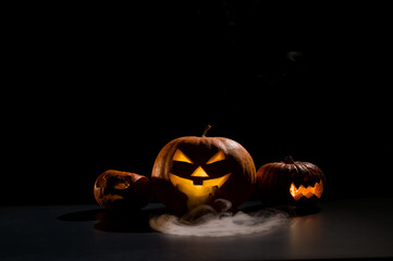 Halloween card. jack o lantern with candles glow on a black background. A row of creepy pumpkins with carved grimaces smokes in the dark.
