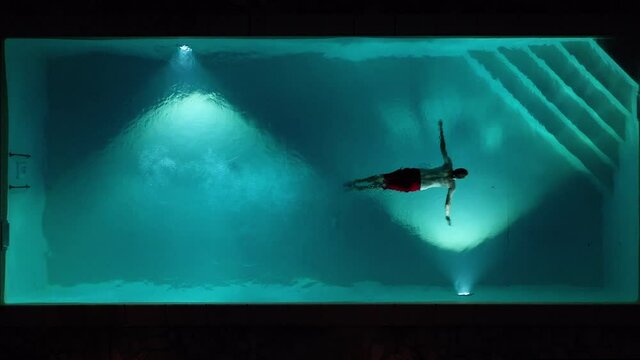 Aerial top shot view of young male adult jumping diving swimming pool at night in tuscany italy shot in 4k