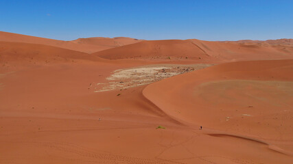 Aerial view of big orange sand dunes with two people walking in the valley at Sossusvlei, Namib desert, Namibia, Africa. Blue sky with no clouds.