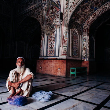 An old man sitting in a mosque with his belongings