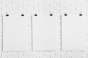 Blank posters hanging on white brick wall