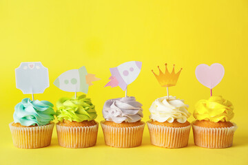 Tasty cupcakes with stylish toppers on color background