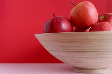 Apples in a wooden plate on a red background.