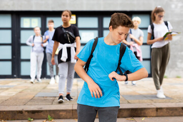 Focused teen student with backpack on back looking at his watch on way to college in autumn day