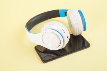White wireless headphones and smartphone on yellow background.