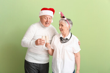 Fototapeta na wymiar Elderly couple with champagne celebrating Christmas on color background
