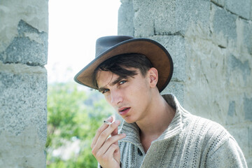 Handsome guy with confident face. Close up young man smoking a cigarette, cigar. Handsome man wear cowboy hat.