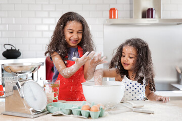 Funny little girls making mess while baking a cake together in kitchen
