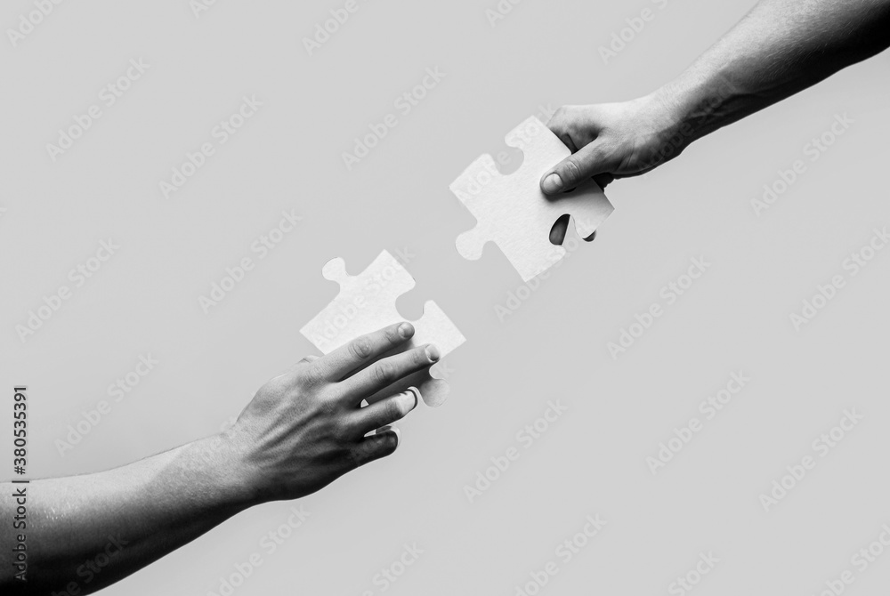 Wall mural Two hands trying to connect couple puzzle. Closeup hands of man connecting jigsaw puzzle. Business solutions, success and strategy concept. Black and white