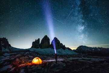 male adventurer with strong headlamp beside illuminated red orange under the milky way at the three pinnacles