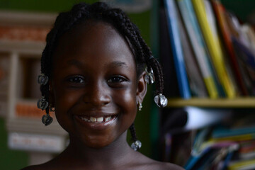 Headshot portrait of a smiling Black girl child on bookshelf background
