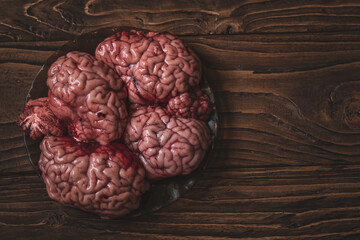 Pink brain before cooking on a plate of dark glass stands on a wooden table.