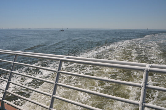 Die Fährfahrt: Das Kielwasser hinter einem Fährschiff. Die Heckreling mit Heckwasser. Die Hecksee mit Geländer. Wasserwirbel und Strudel bewegen das Meer. Es entsteht eine Kielspur.