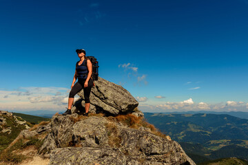 Young man with a backpack standing on top of a mountain and enjoying the view of the valley, the top of the Carpathians Eared stone.