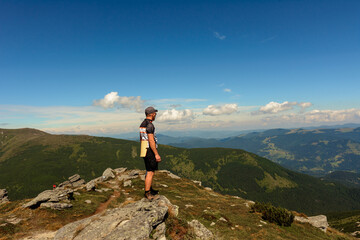 traveler, tourist, traveler stands on top of a cliff and enjoys a sunny day and a view of the picturesque Carpathians.
