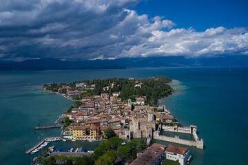 Naklejka premium Aerial view on Sirmione sul Garda. Italy, Lombardy. Cumulus clouds over the island of Sirmione. Aerial photography with drone. Panoramic view at high altitude. Rocca Scaligera Castle in Sirmione.