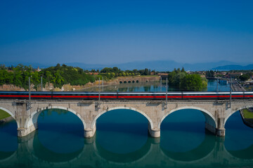 Train passing over the bridge that crosses the reservoir Blurred train movement on arch bridge over the river against the background of mountains.