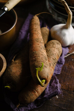 Closeup of unwashed carrots and garlic on wooden background.