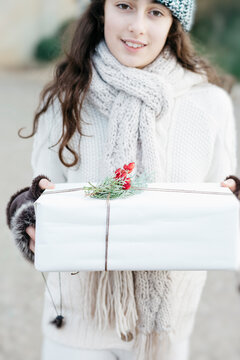 Preteenager girl holding a Christmas gift box and looking at camera