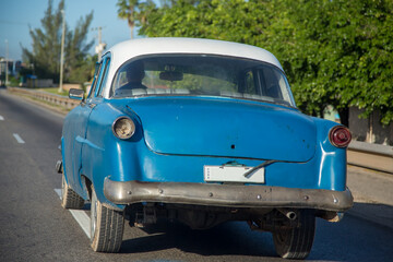 An old beaten up car driving on the road in Cuba.