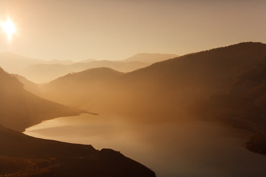 Beautiful sunset above the lake and mountains covered with light fog