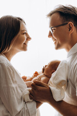 Portrait of happy parents with newborn baby, beautiful mom hold little daughter in arms, loving wife looking at caring husband, smiling, enjoy tender moments, young family concept