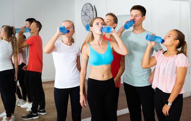 Healthy active teens relaxing on break during dancing training, drinking water with young female trainer