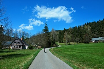 Fototapeta na wymiar Czech Republic - view of a cyclist and a wooden house in the Antonina valley in the spring near the town of Svoboda
