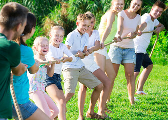 Active kids with moms and dads playing tug of war during joint outdoors games on sunny day