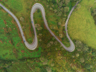 Winding narrow road on a hill in Burren, Ireland. Aerial drone view. Green fields and small trees around the pass.